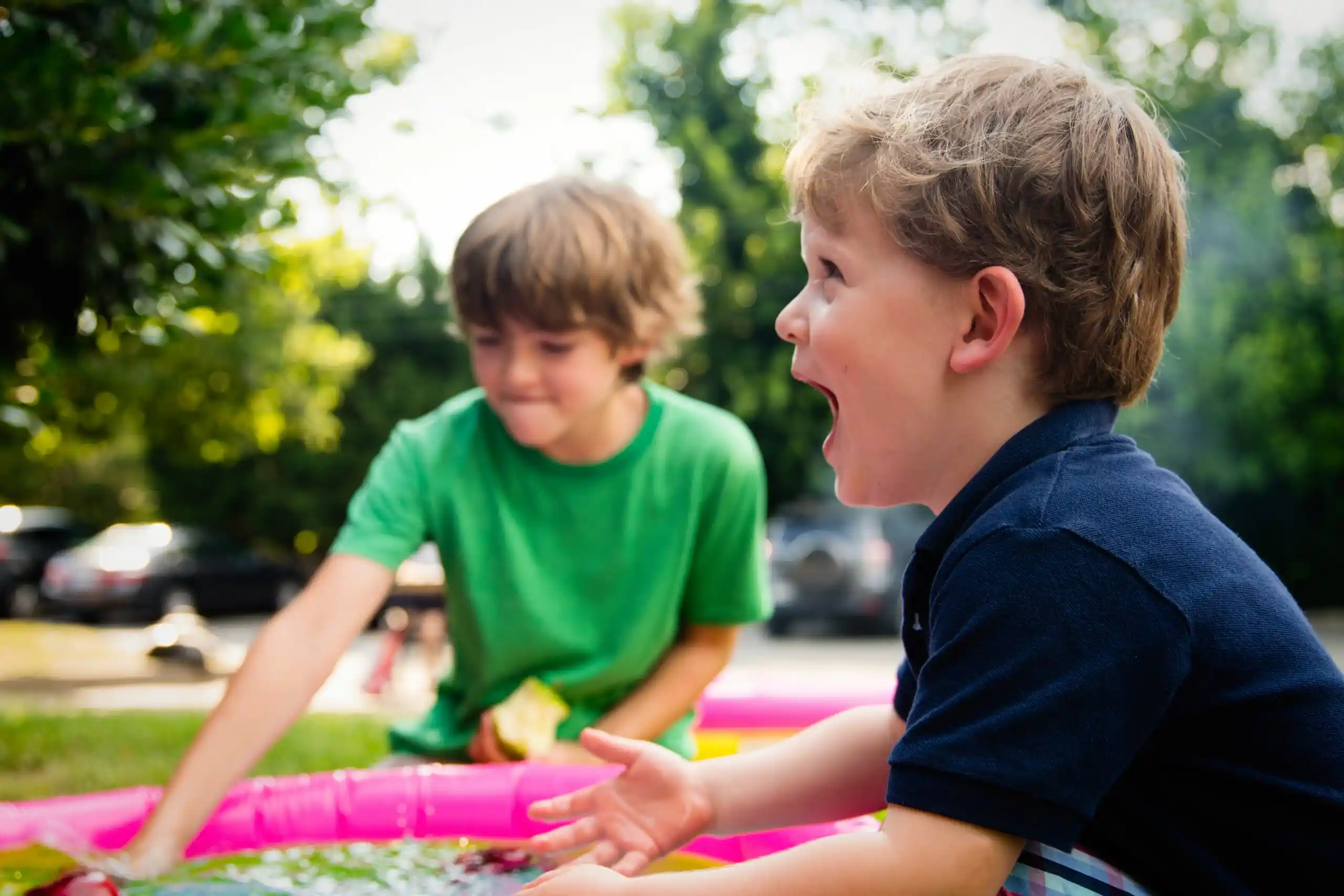Two children play amongst trees with a slip-and-slide pool